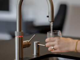 Quooker Wasserhahnen mit sprudelndem kühlen Wasser. Frau hält Glas unter den Wasserhahnen.